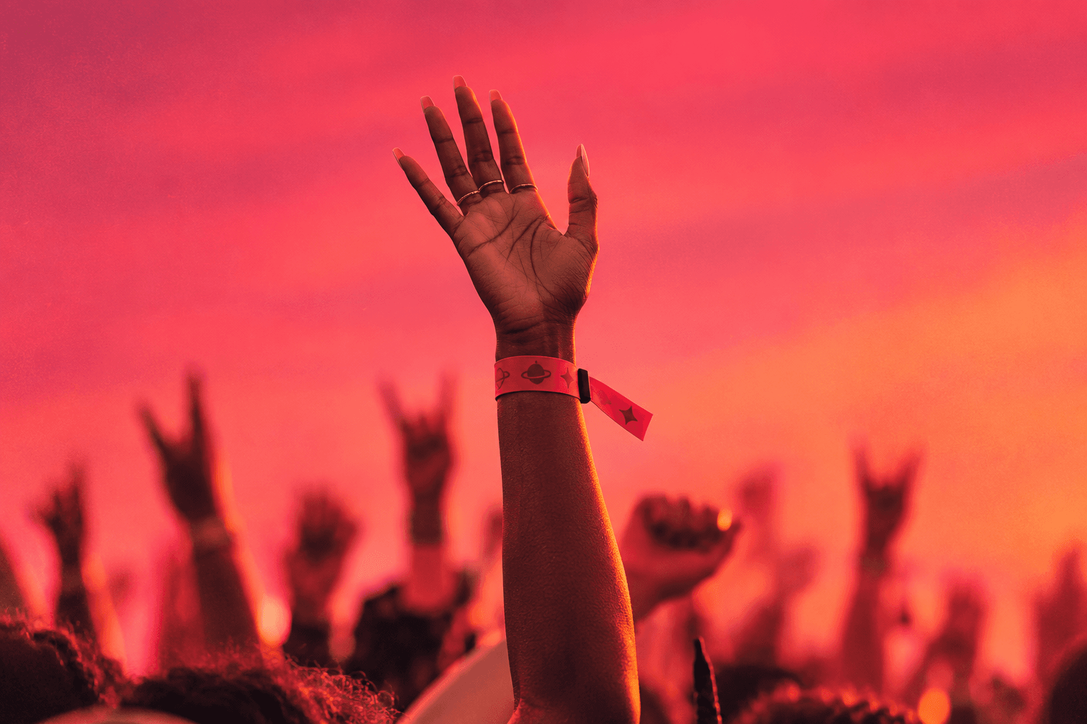 A raised hand wearing a LiveTags wristband above a festival crowd